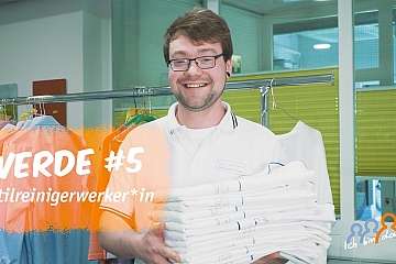 Ein lächelnder Textilreiniger hält einen Stapel sauberer Wäsche.